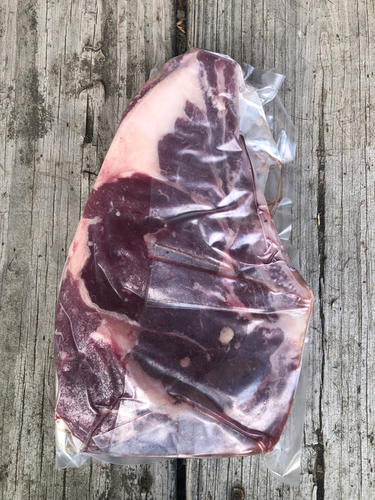 A vacuum-sealed raw cut of marbled beef bone-in ribeye steak, placed on a weathered gray wooden surface.