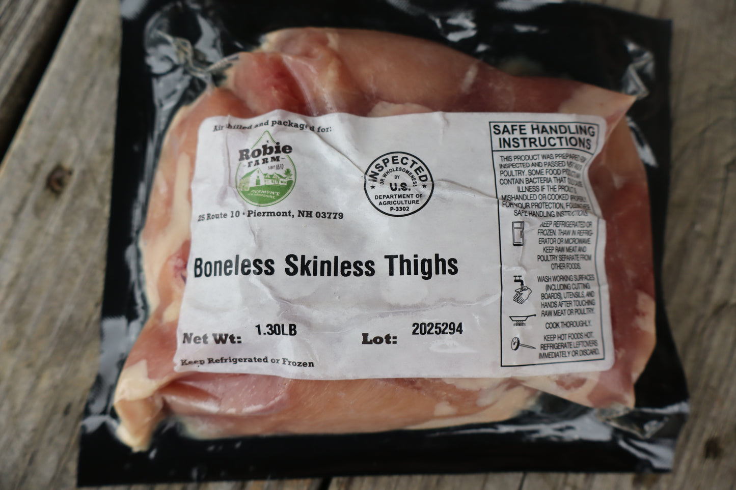 Packaged Robie boneless skinless chicken thighs with a label on a wooden surface