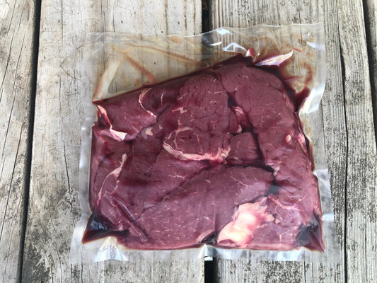 Raw marbled beef loin top sirloin steak tips from Robie Farm inside a clear plastic vacuum-sealed bag, placed on a weathered gray wooden surface.
