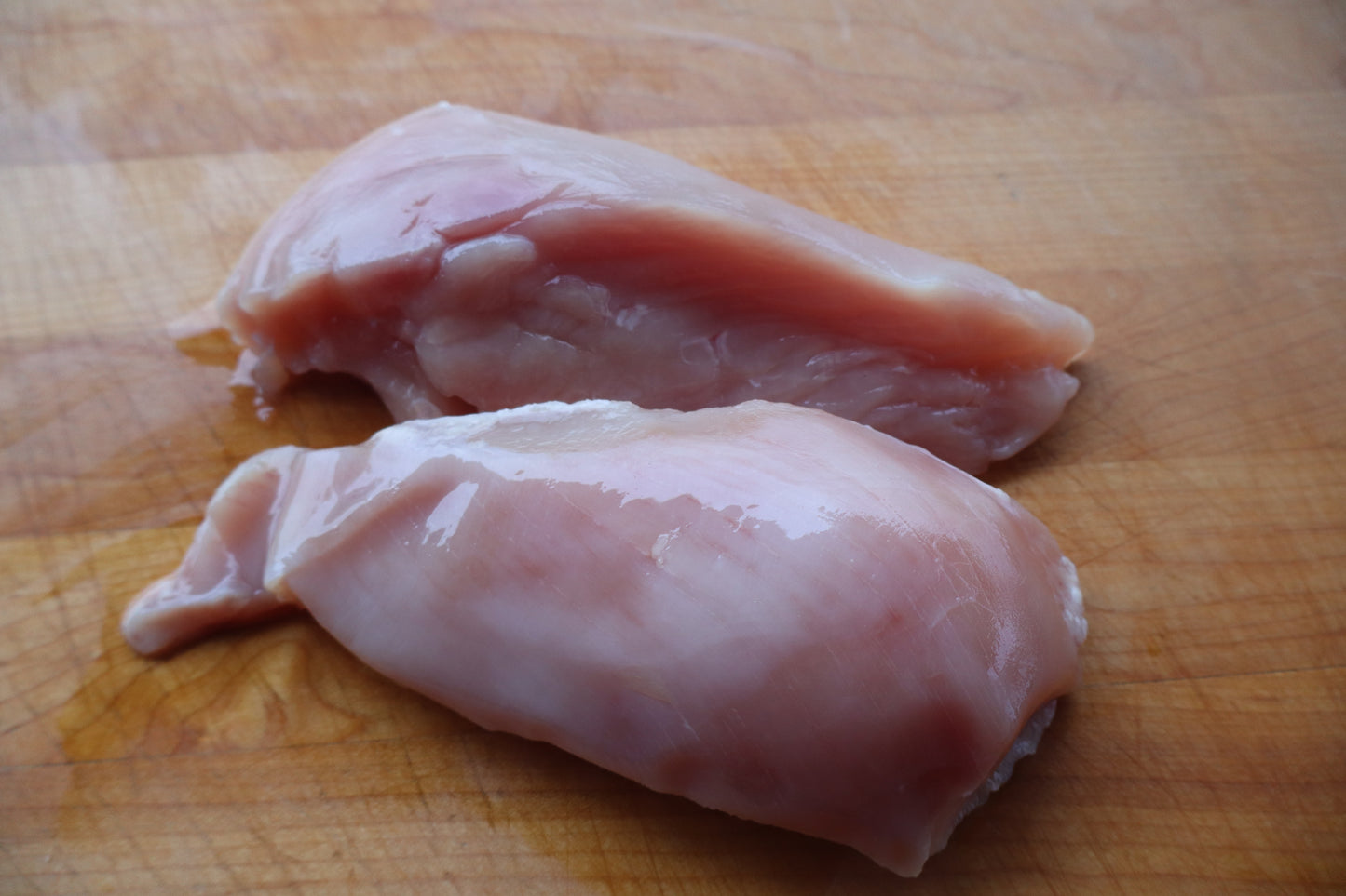 Two pieces of raw Robie Farm chicken breast on a wooden cutting board.