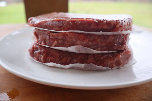 Stack of ground Robie beef patties on a white plate with a blurred background