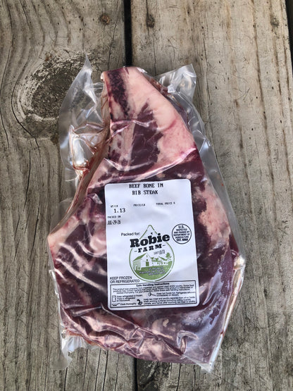 A vacuum-sealed cut of beef bone-in ribeye steak from Robie Farm in Piermont, NH resting on a wooden surface