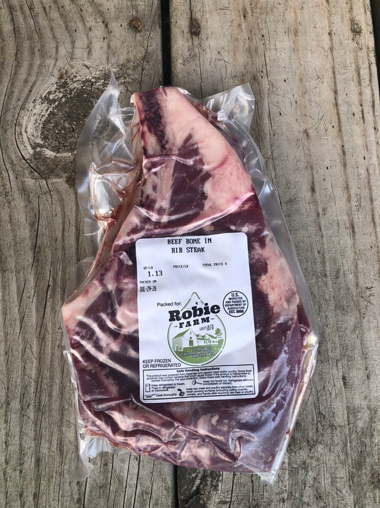 A vacuum-sealed cut of beef bone-in ribeye steak from Robie Farm in Piermont, NH resting on a wooden surface