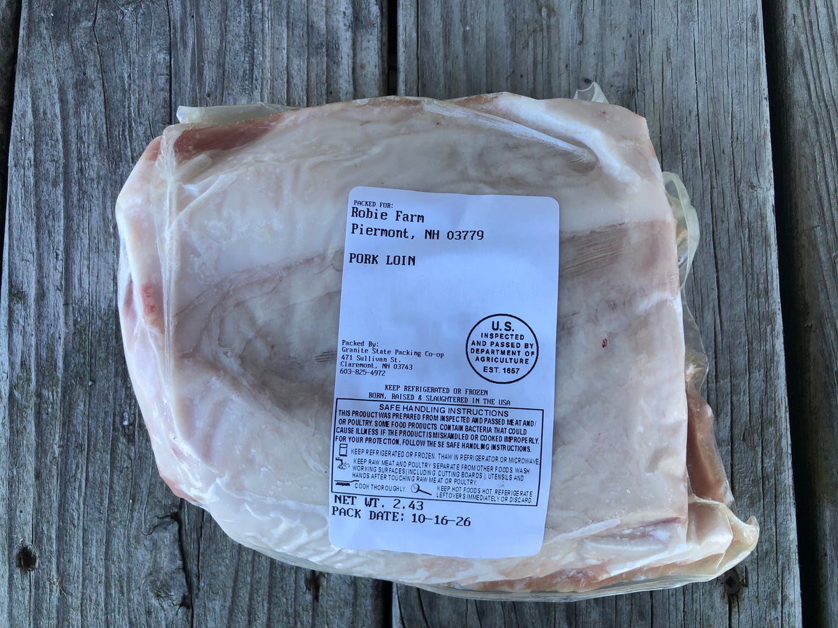 A vacuum-sealed package of raw boneless pork loin resting on a weathered gray wooden surface. The package has a white label with black text detailing the product information, including the brand ‘Robie Farm' and location 'Piermont, NH'.