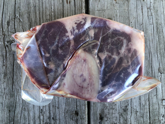 A vacuum-sealed package of Robie Farm cross cut beef shank placed on a weathered gray wooden surface.