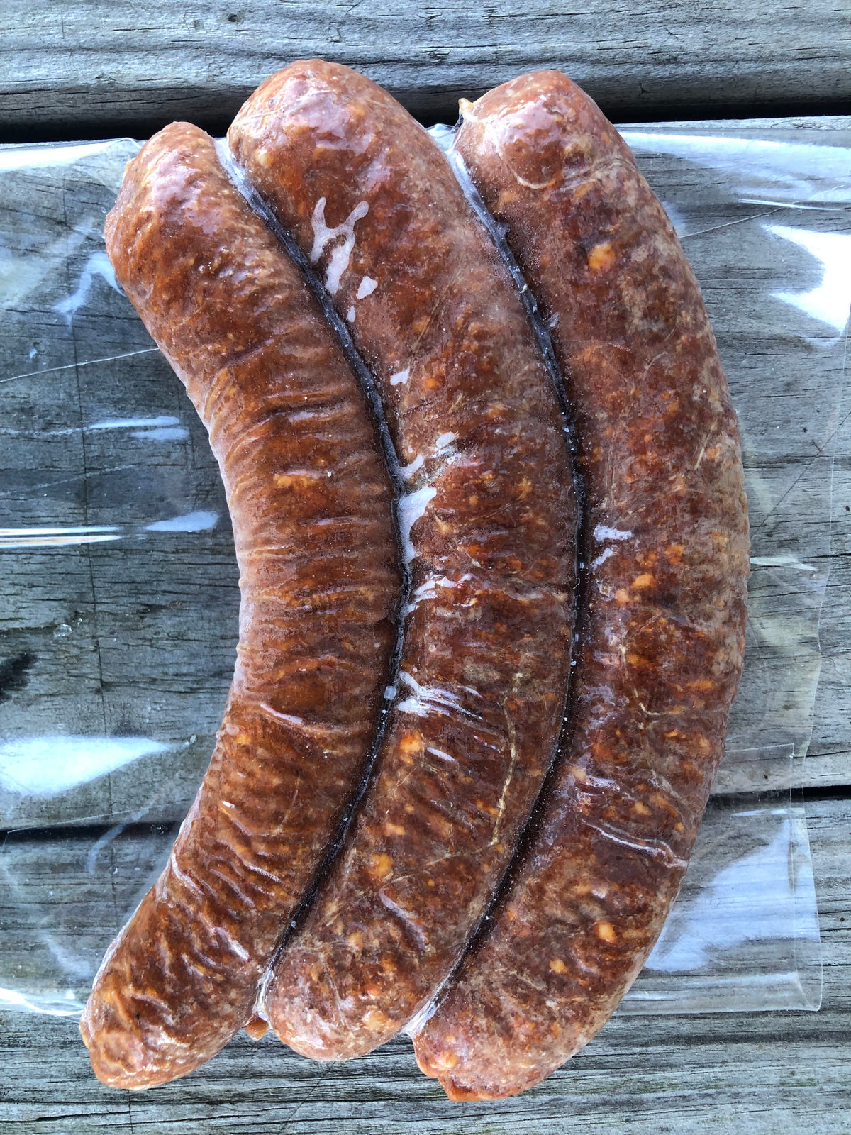 Three raw pork sausages in freezer vacuum sealed bag on a weathered gray wooden surface.