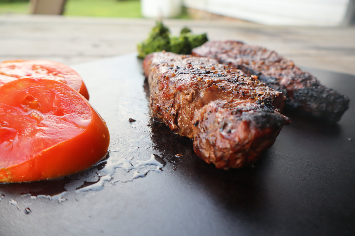 Grilled steak with sliced tomatoes on a dark surface