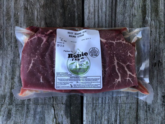 A vacuum-sealed package of Robie Farm beef eye round steaks, placed on a weathered gray wooden surface.