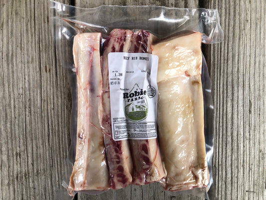 Grass fed and grain finished beef rib bones in a package resting on a faded wooden table