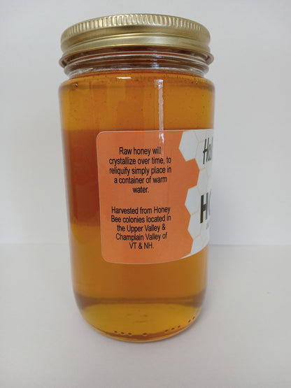 A glass jar of raw honey from Hall Apiraries with a gold metal lid and a white and orange label, photographed against a plain white background.