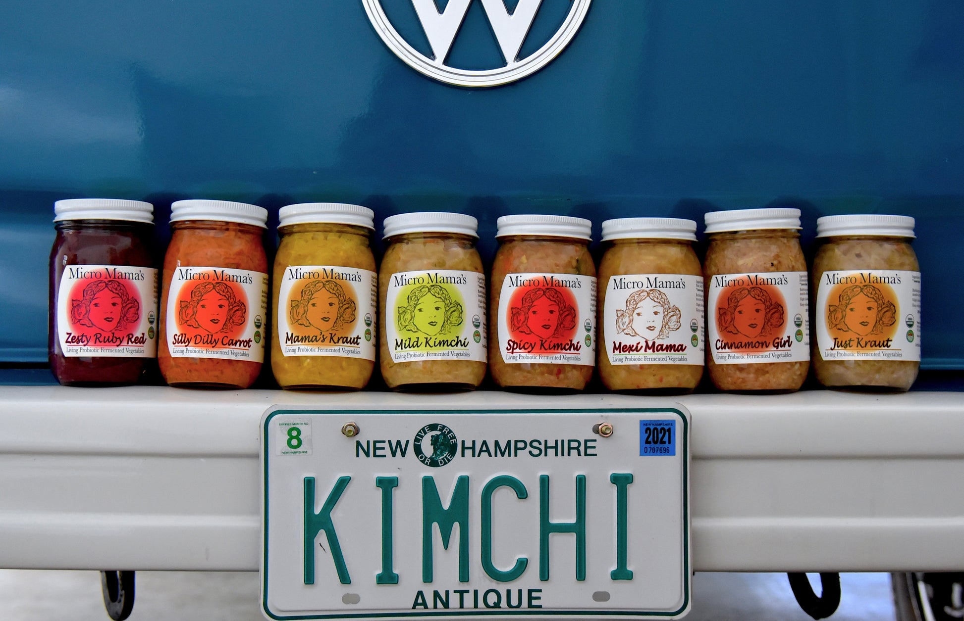 Row of Micro Mama's fermented vegetable products in jars on the bumper of an antique care with a New Hampshire license plate that reads Kimchi