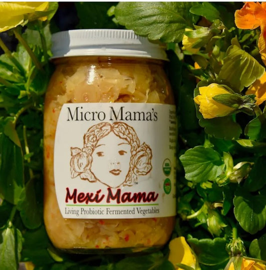 Jar of 'Micro Mama's Mexi Mama' probiotic vegetables surrounded by green leaves and yellow flowers.