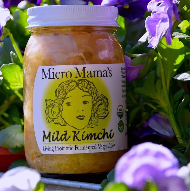 Jar of Micro Mama's Mild Kimchi surrounded by greenery and purple flowers