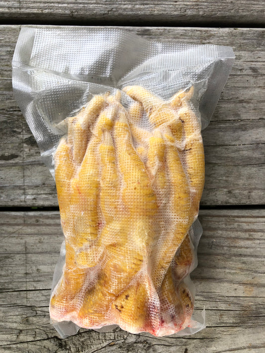 Frozen chicken feet in a clear vacuum-sealed bag placed on a weathered wooden surface.