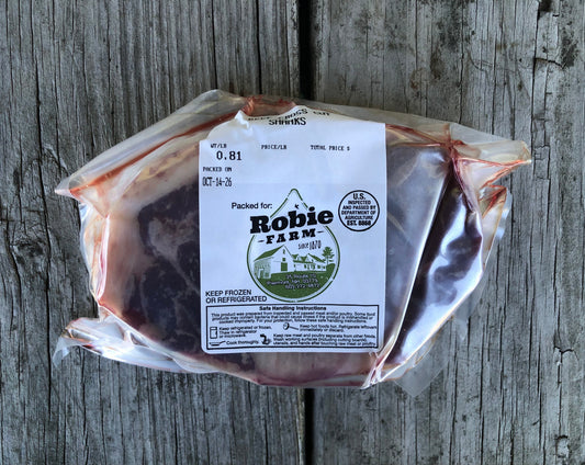 A vacuum-sealed package of Robie Farm raw beef cross cut shank resting on a weathered gray wooden surface.