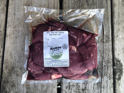 A vacuum-sealed package of Robie Farm beef loin top sirloin for steak tips, placed on a weathered gray wooden plank surface.
