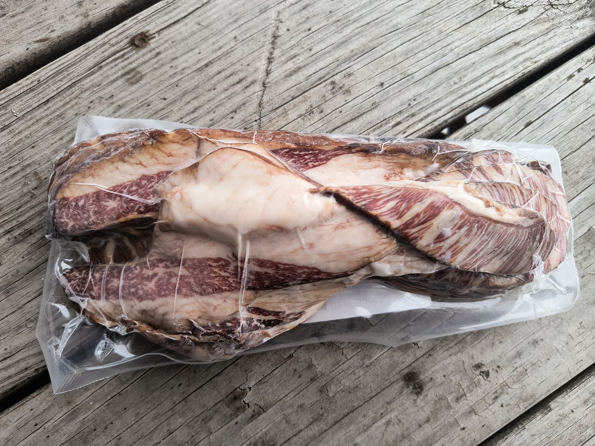 Vacuum-sealed package of uncured beef bacon resting on a wooden surface