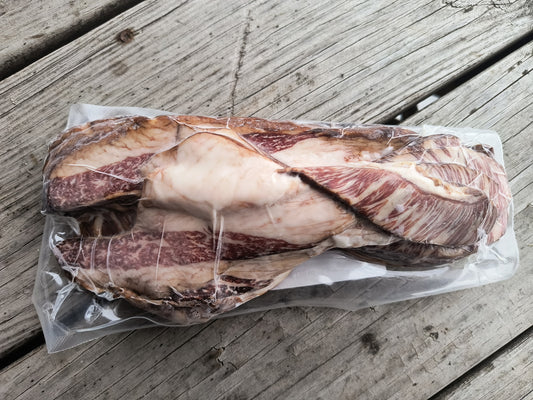 Vacuum-sealed package of uncured beef bacon resting on a wooden surface