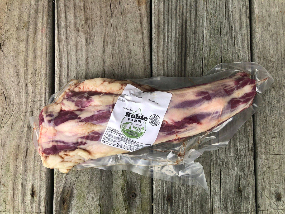 A vacuum-sealed cut of raw Robie Farm beef ox tail with marbling, featuring a white paper label, placed on a rustic gray wooden plank surface.