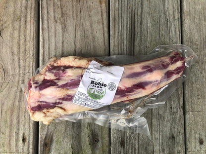 A vacuum-sealed cut of raw Robie Farm beef ox tail with marbling, featuring a white paper label, placed on a rustic gray wooden plank surface.
