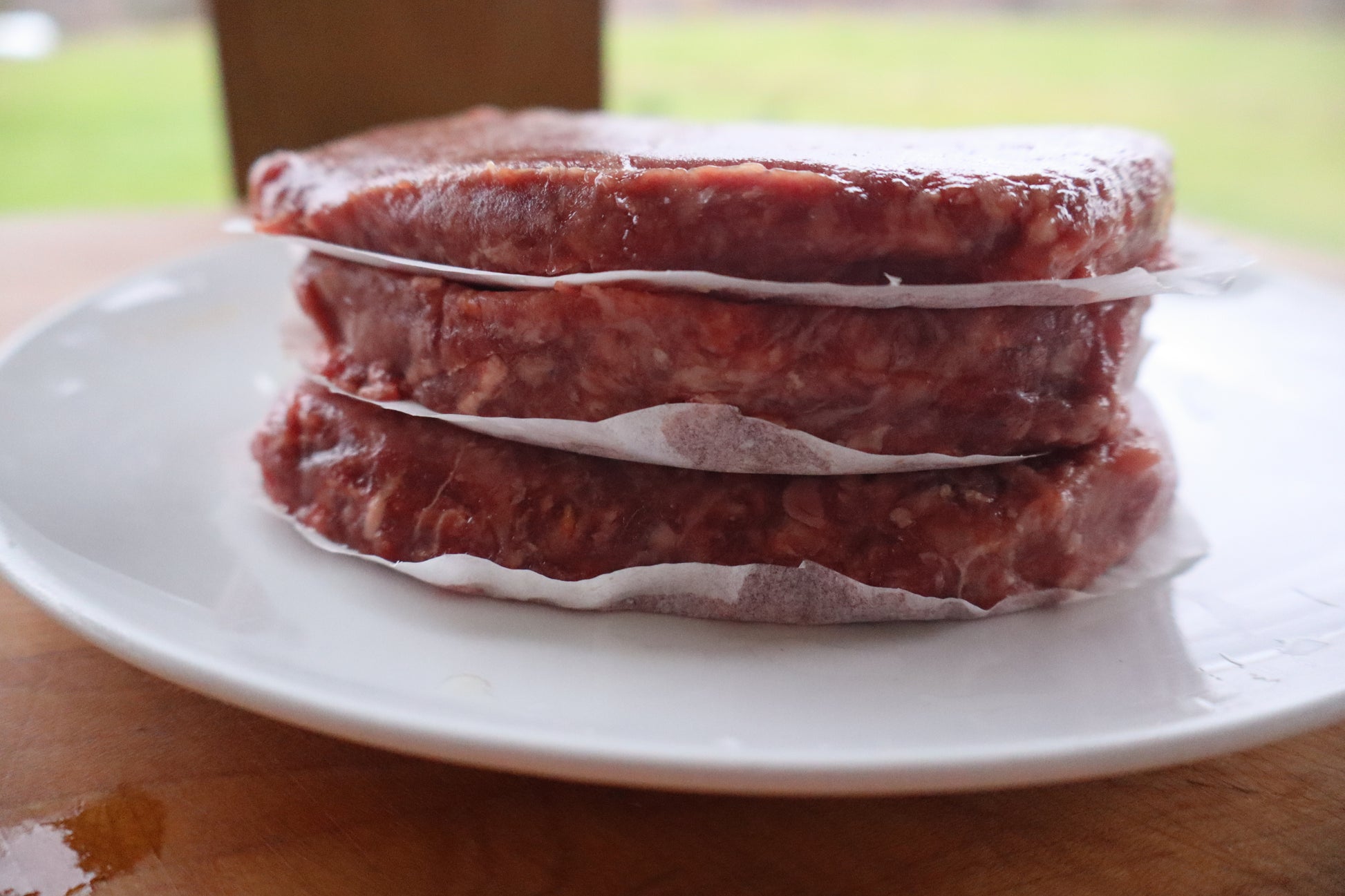 Stack of ground Robie beef patties on a white plate with a blurred background