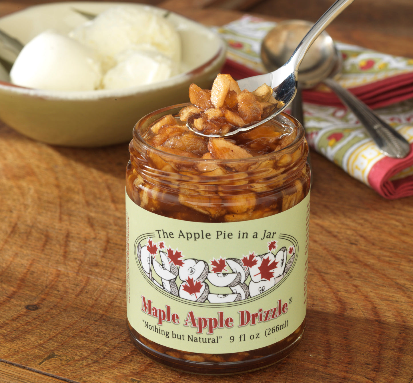 An open jar of Side Hill Farm Maple Apple Drizzle with a spoon sampling the contents