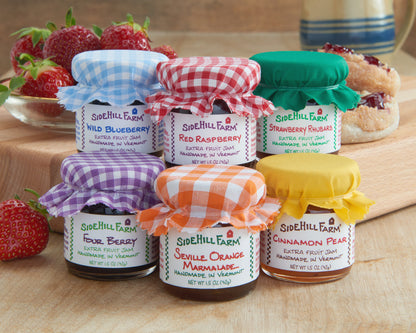 Assorted jars of Sidehill Farm jam on a wooden surface with strawberries and pastries.